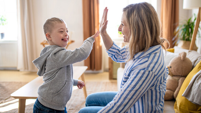 Eine fröhliche, junge Mama spielt mit ihrem Sohn mit Downsyndrom zu Hause