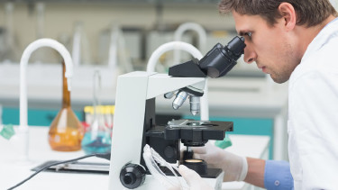 Mann in Laborkleidung blickt durch ein Mikroskop
