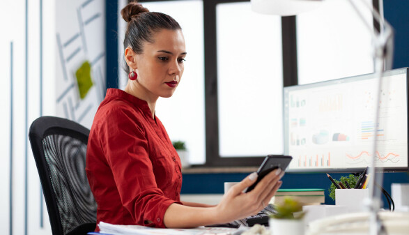 Frau sitzt im Büro und schaut auf ihr Handy