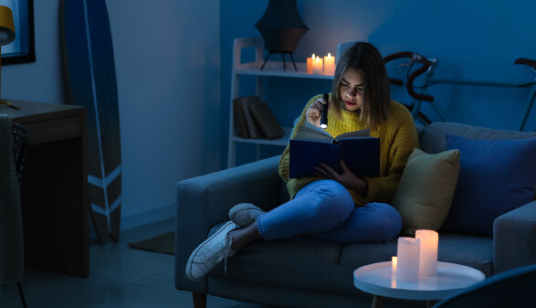 Frau sitzt in dunklem Zimmer und liest mit Taschenlampe ein Buch