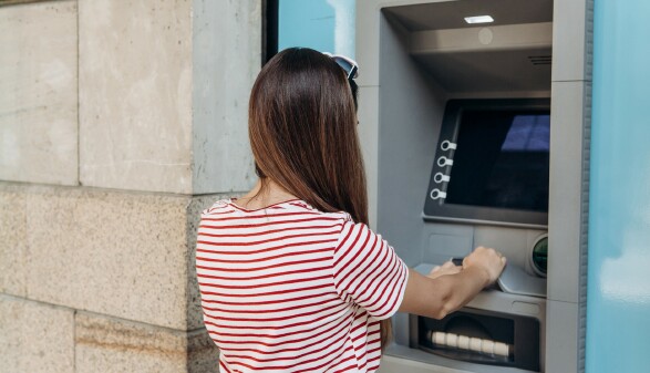 Junge Frau hebt beim Bankomaten Geld ab.