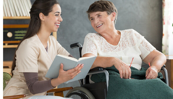 Betreuerin liest Frau im Rollstuhl vor