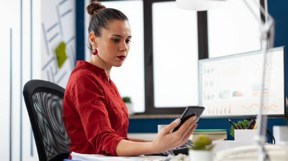 Frau sitzt im Büro und schaut auf ihr Handy