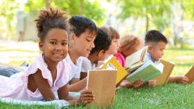 Kinder liegen gemeinsam auf der Wiese und lesen.