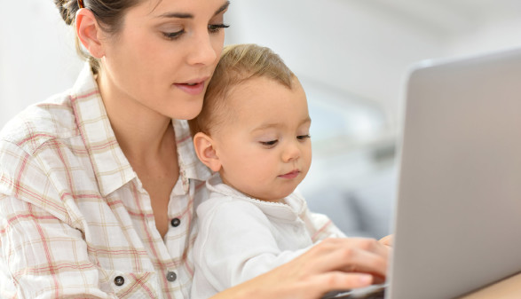 Mutter mit Kleinkind schreibt am Laptop