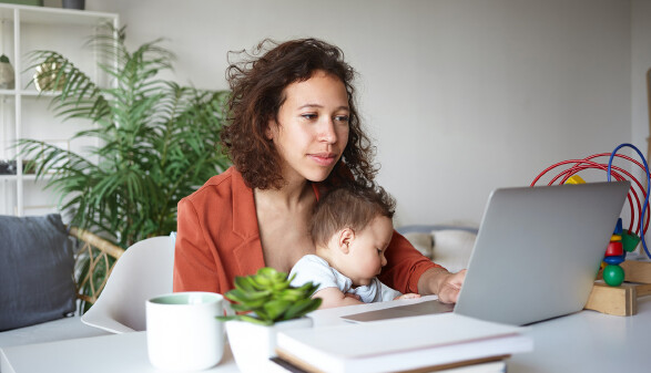Frau mit Baby am Schoß arbeitet am Laptop