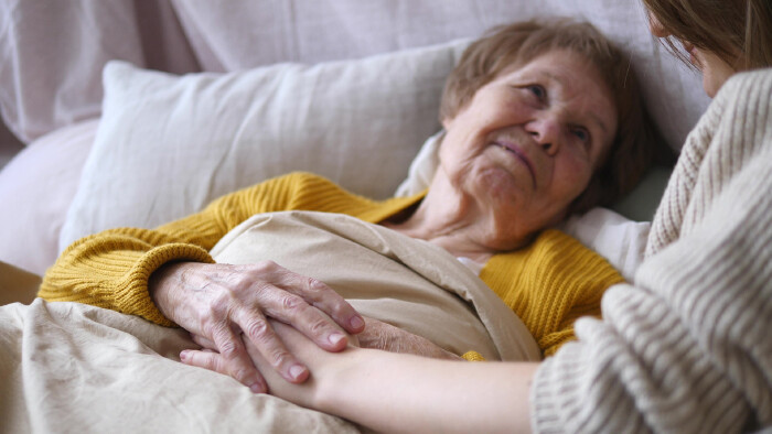 Alte Frau liegt im Bett und hält die Hand einer jüngeren Frau