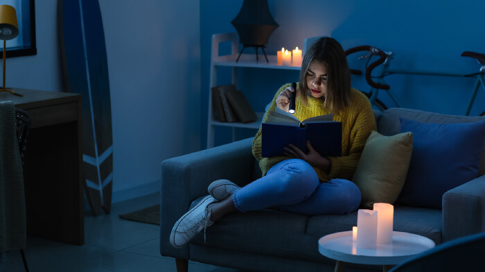 Frau sitzt in dunklem Zimmer und liest mit Taschenlampe ein Buch