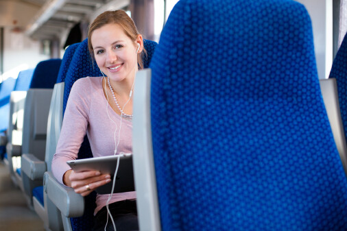 Frau reist mit Tablet in der Hand und Kopfhörern in den Ohren im Zug